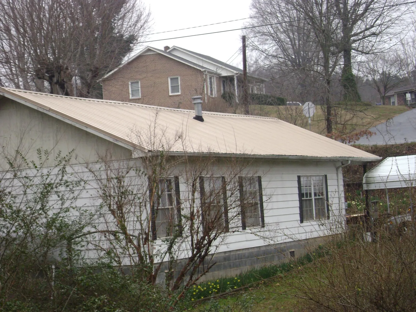 Tan metal roof on a white sided house set into a hillside — Commercial Roofing by Roofing Brothers in Ocean Park